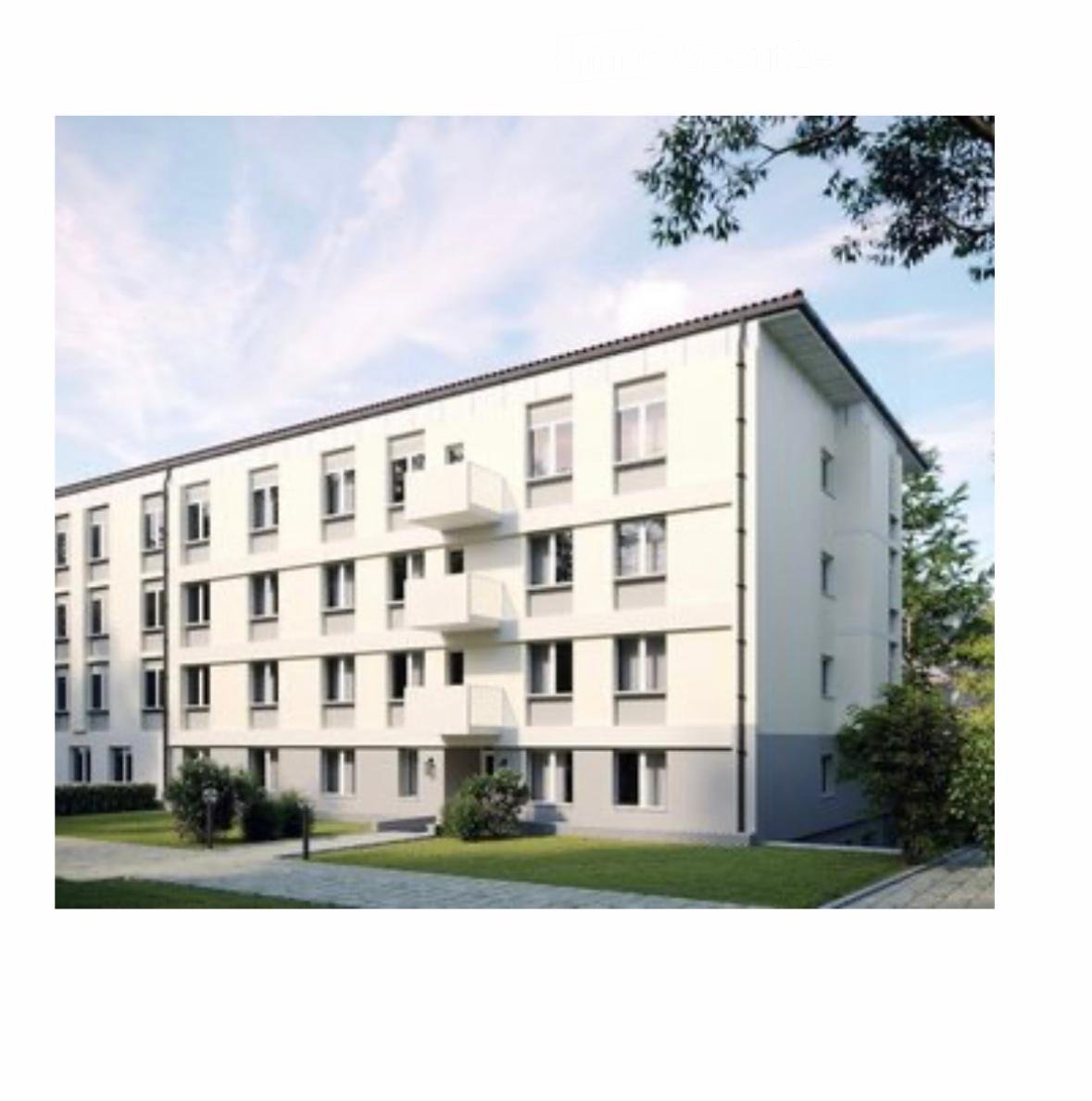 Modern multi-story residential building with white facade, multiple windows, and balconies. The building is surrounded by a well-maintained lawn and small shrubs.