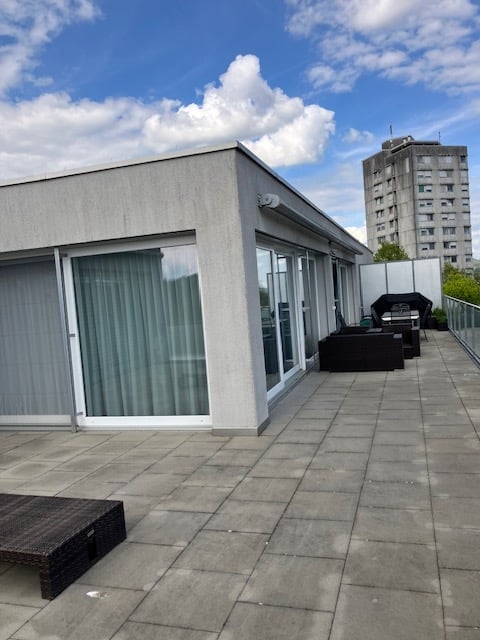 Roof terrace with large sliding glass doors, tiled floor, and outdoor furniture including a sofa and a table.