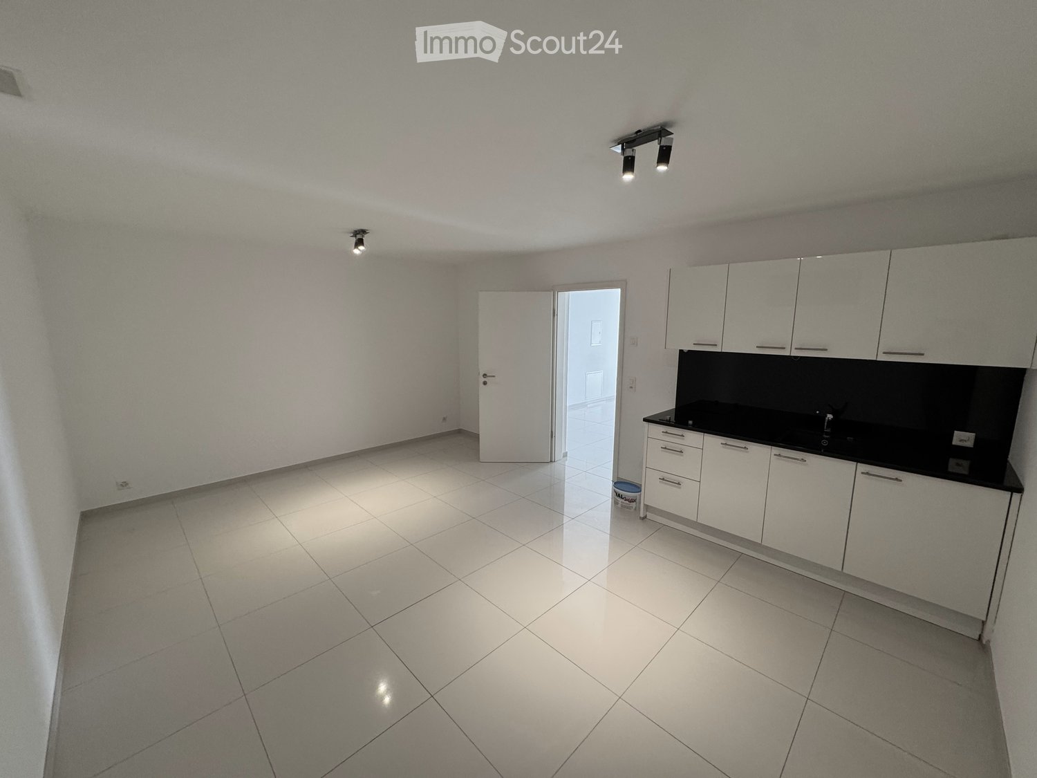 Empty kitchen with white tiled floor, white cabinets, and a black countertop. No appliances or furniture are present.