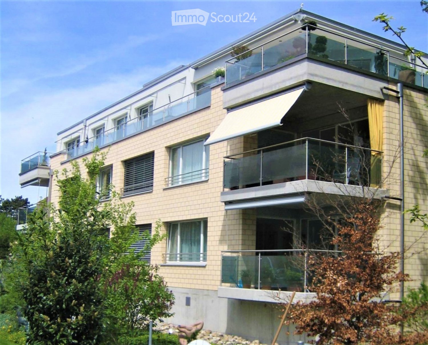 Modern3-story building with beige brick facade, large windows, and multiple balconies with glass railings.