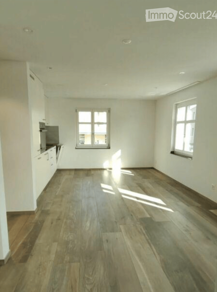 Empty room with wooden flooring, white walls, and two windows allowing natural light to enter. The room is unfurnished, showing only the basic structure and lighting fixtures.