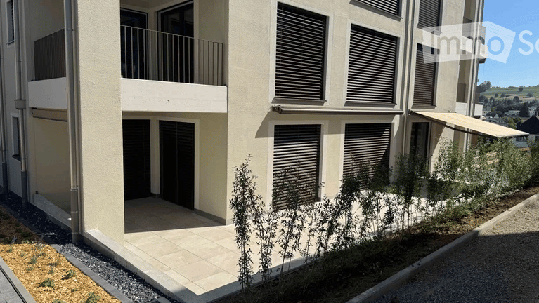Modern multi-story residential building with balconies, large windows, and a covered entrance area.