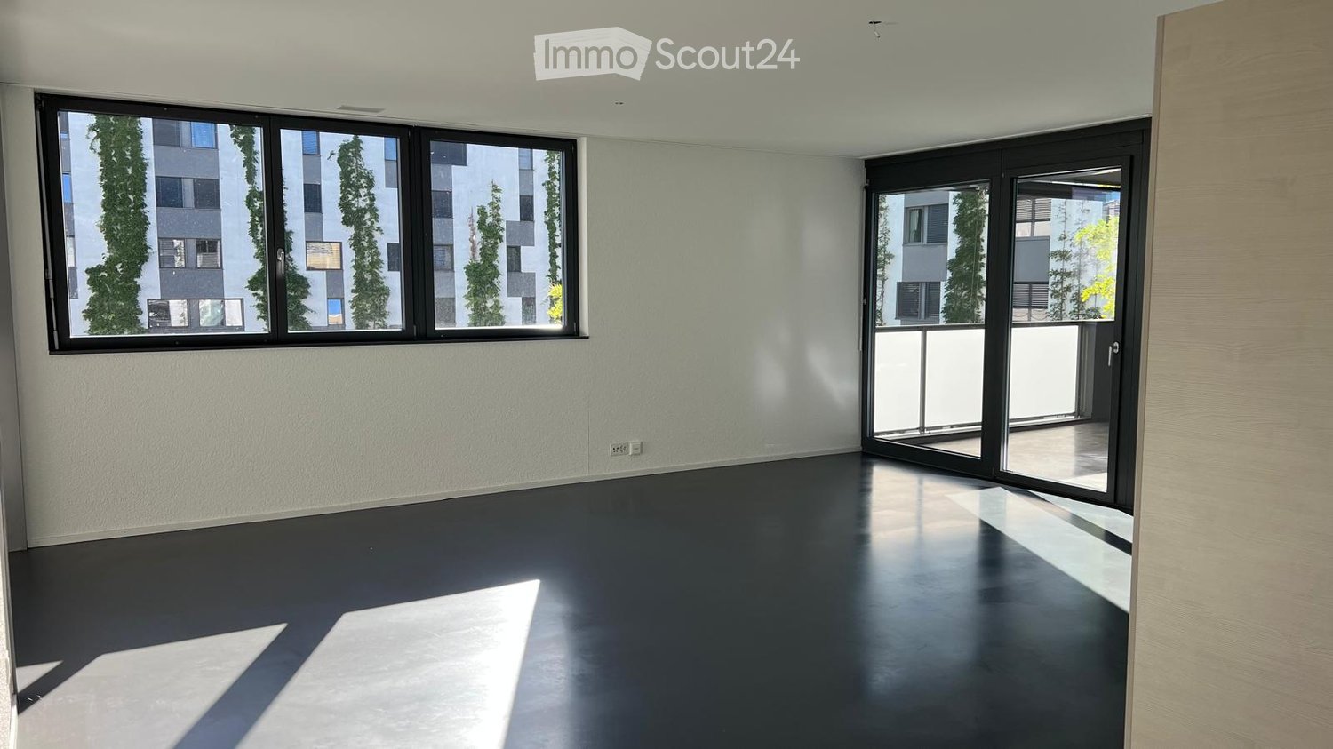 Empty room with dark flooring, large windows, and a sliding glass door leading to a balcony.