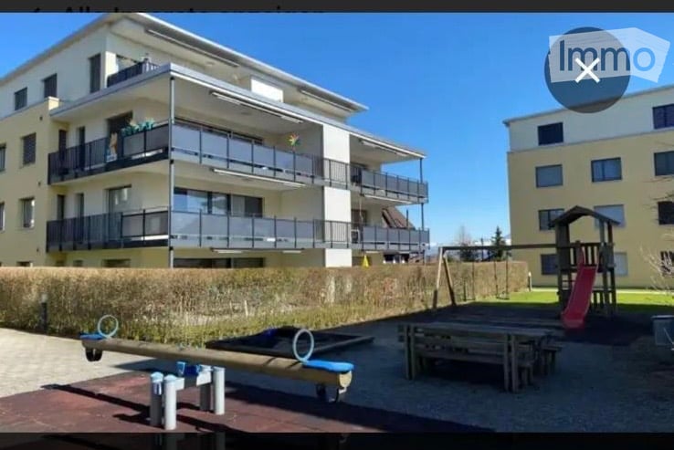 Modern multi-story residential building with multiple balconies and a playground area in front.