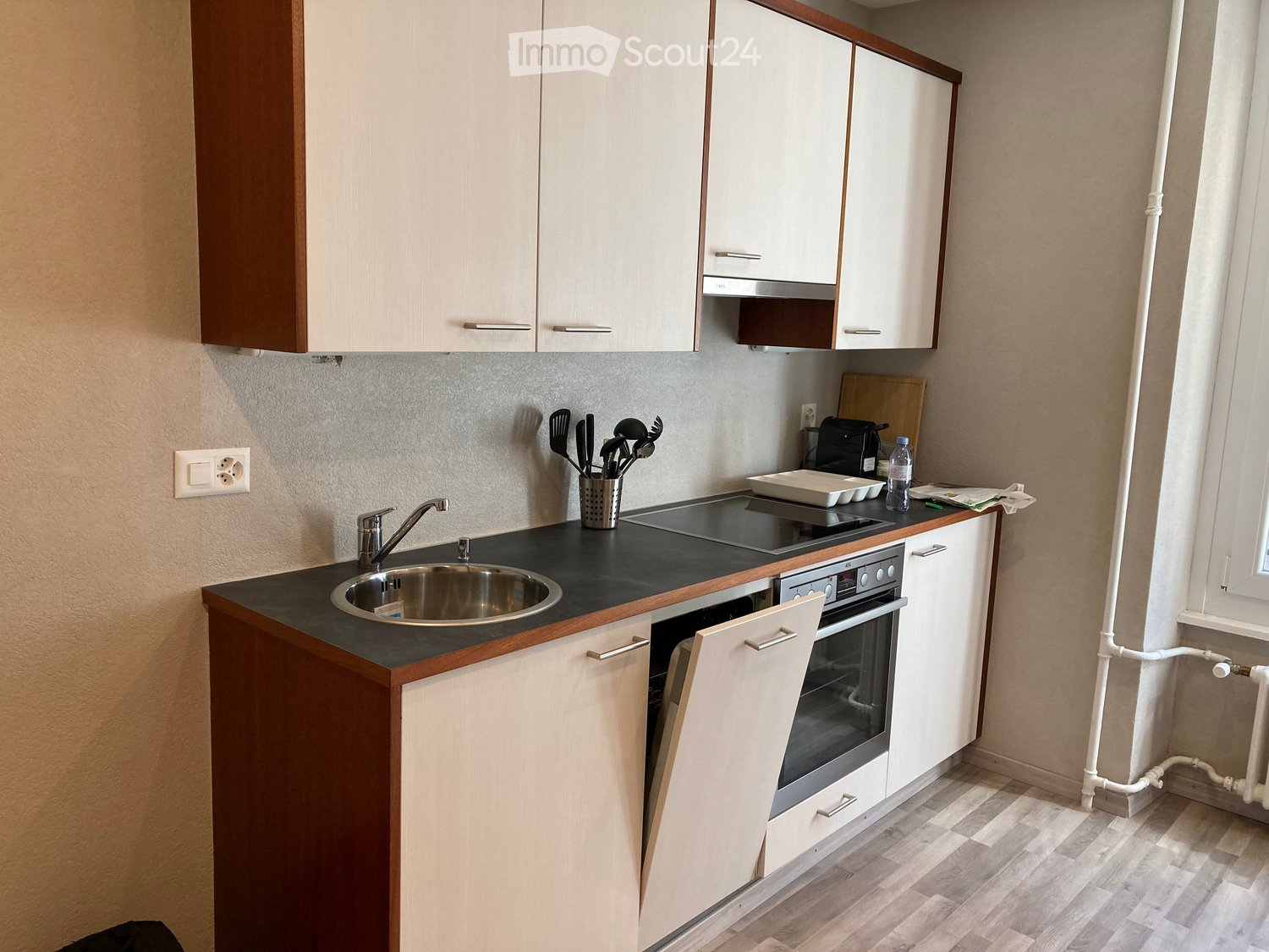 Modern kitchen with white cabinets, a stainless steel sink, an oven, and a countertop with various utensils and appliances.