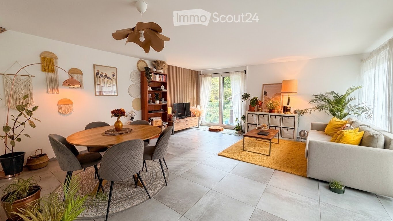 Modern living and dining area with a grey sofa, wooden coffee table, round dining table with four chairs, TV stand, bookshelf, and decorative plants.