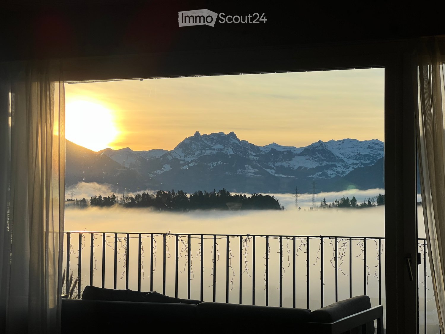 Balcony with a sofa, overlooking a mountain range at sunset with a misty valley below.