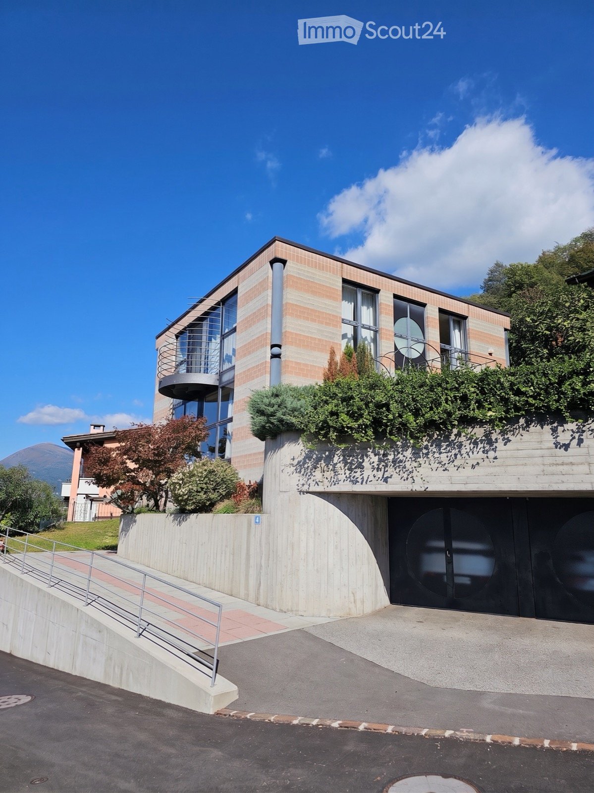 Modern two-story building with brick and glass facade, curved balcony, and landscaped rooftop garden.