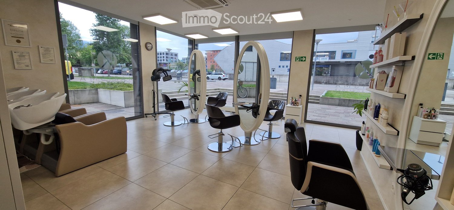 Modern salon with multiple salon chairs, large mirrors, sinks, shelves with hair products, and a hair dryer. Large windows provide natural light and a view of the street.