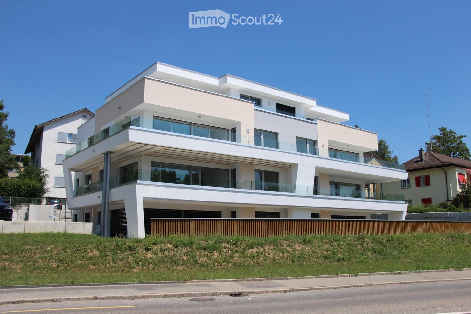Modern two-story house with white exterior, large glass windows, and balconies. Features a raised ground floor and contemporary design.
