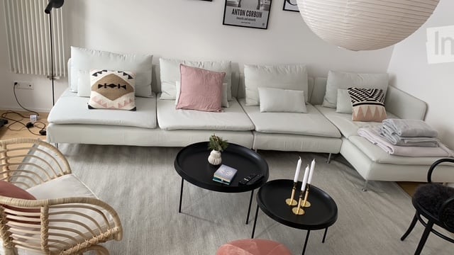 Modern living room with a white sectional sofa, decorative pillows, a black coffee table, side tables, and a wicker chair.