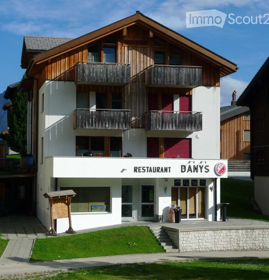 A multi-story building with a restaurant sign reading "RESTAURANT DANY'S" at the base, featuring balconies on the upper floors and a well-maintained lawn in front.