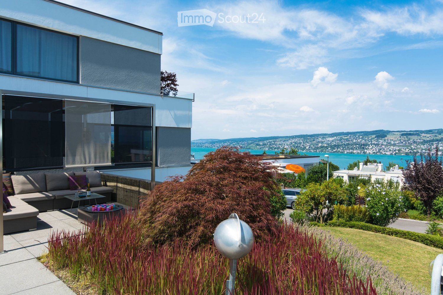 Modern outdoor terrace with a sofa, coffee table, fire pit, and scenic view of a lake and cityscape.