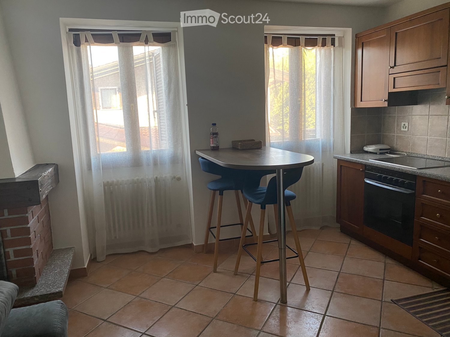 Kitchen with tiled floor, wooden cabinets, a small round table with two blue stools, and a bottle on the table.