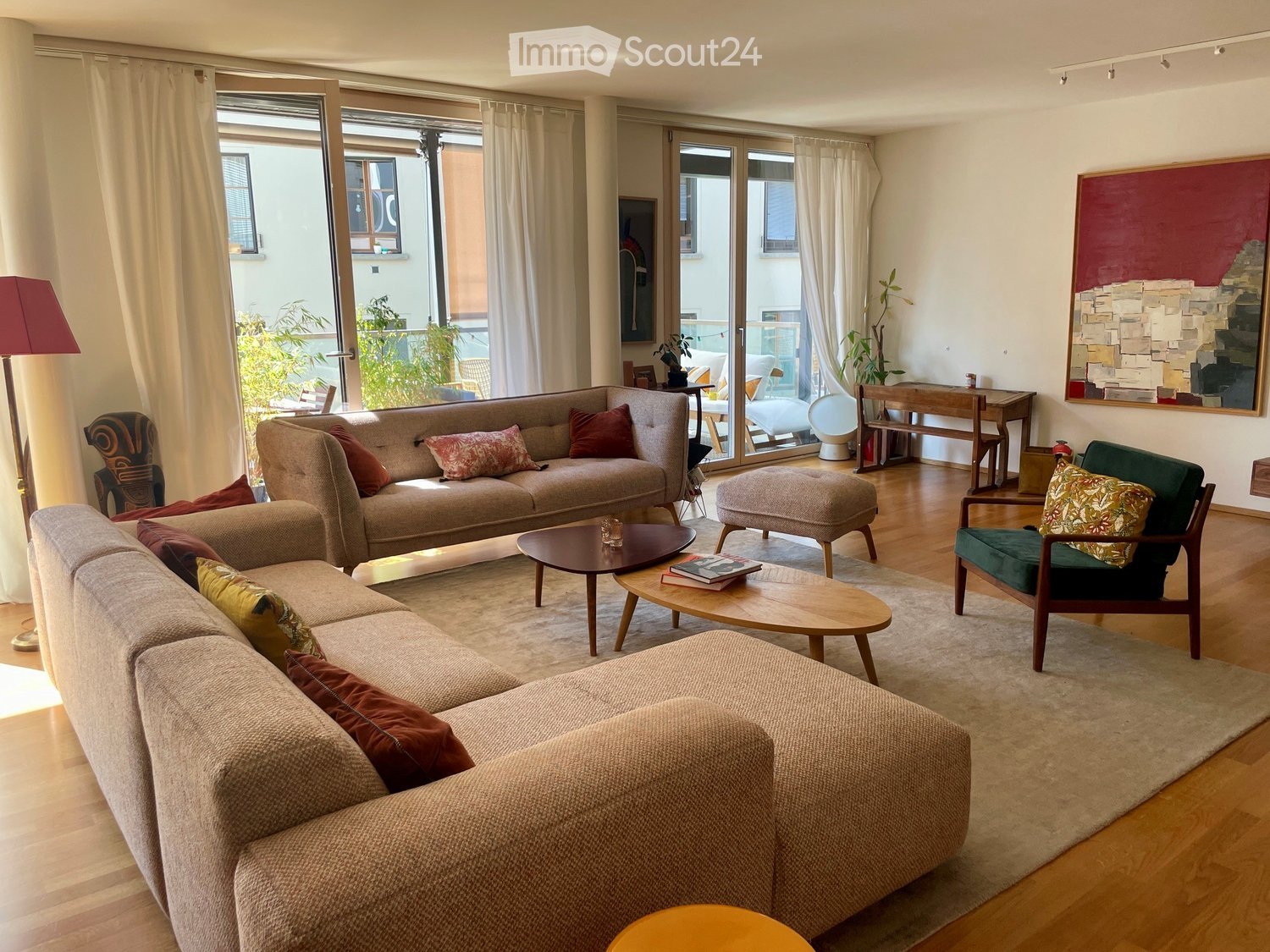Modern living room with large windows, light-colored sofas, coffee tables, ottoman, and artwork on the wall.