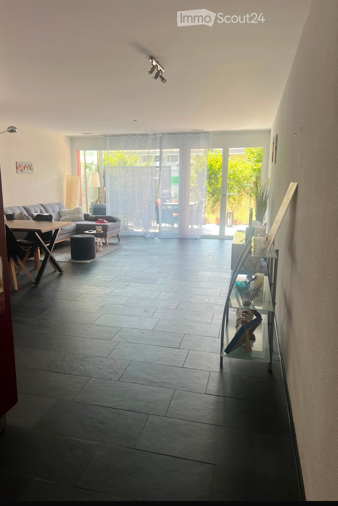 Modern living room with grey sofa, coffee table, glass shelf, and large sliding glass doors leading to a patio.