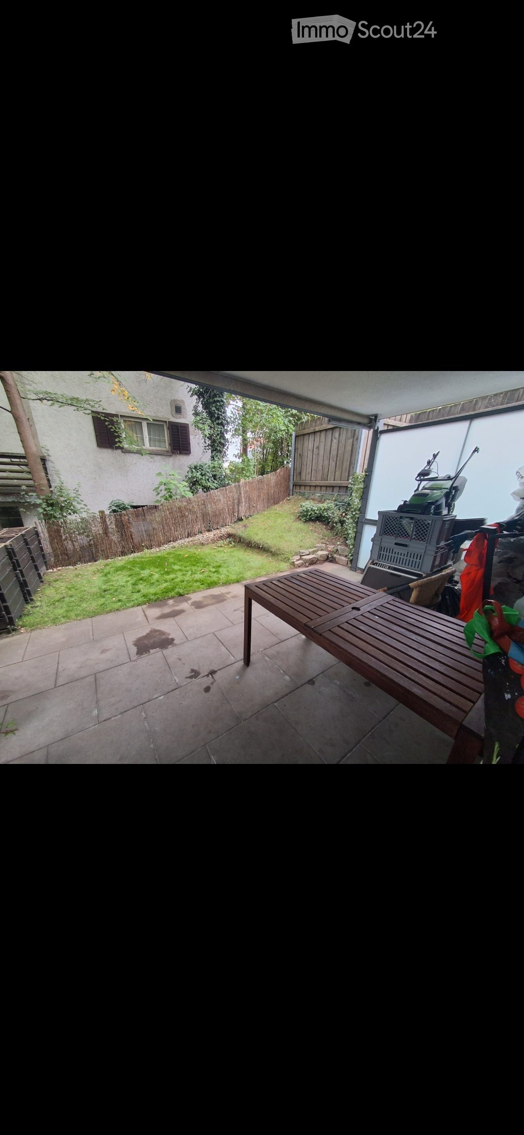 Patio area with tiled floor, wooden bench, grassy lawn, wooden fence, and neighboring house visible.