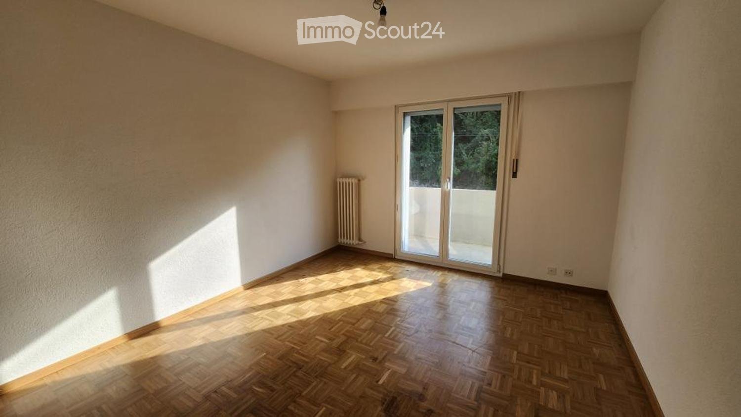 Empty room with wooden flooring, white walls, and a large sliding glass door leading to a balcony.