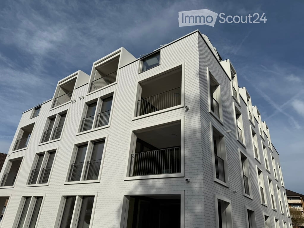 Modern multi-story building with white brick facade, multiple balconies, and large windows.