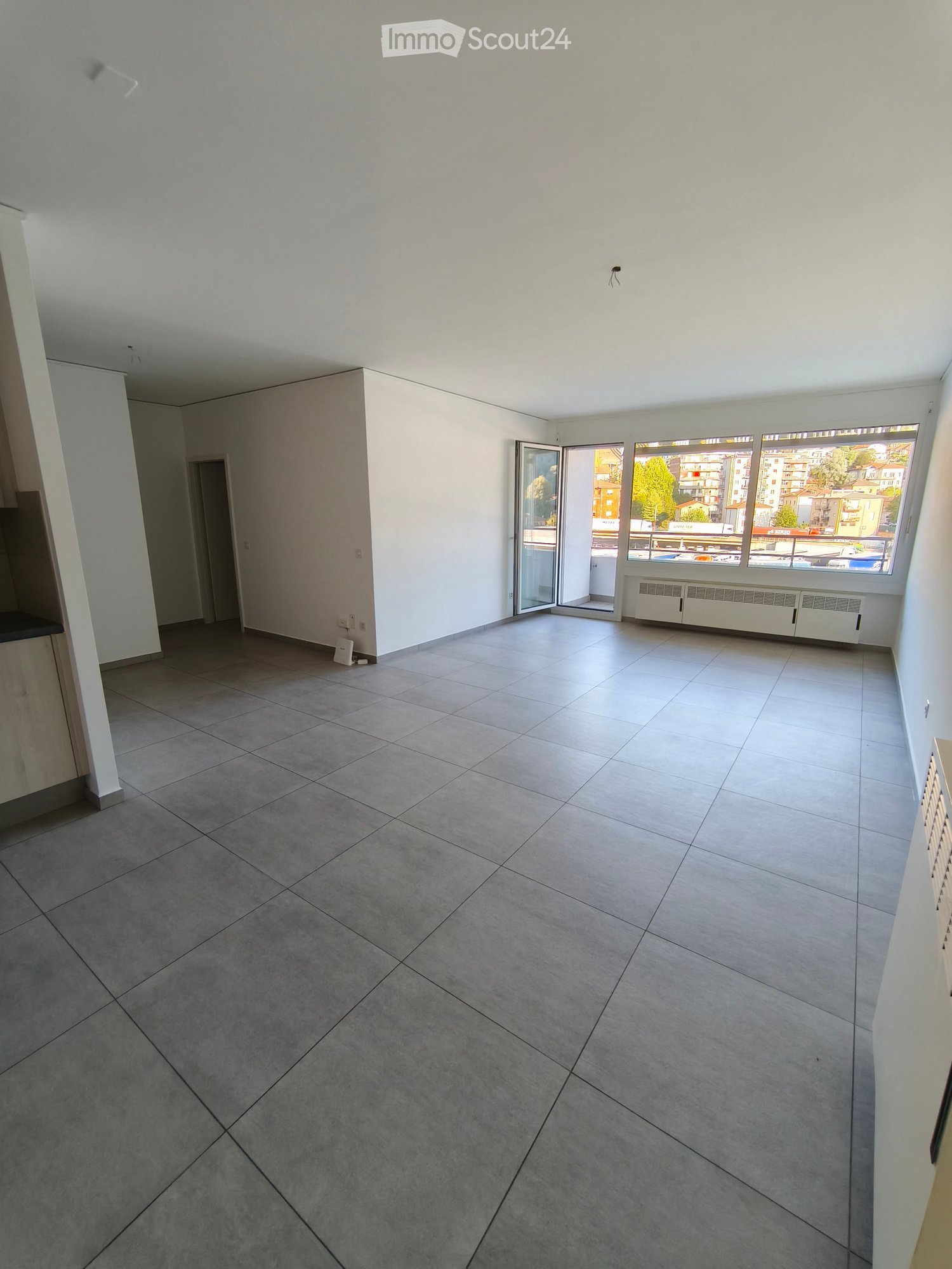 Empty room with tiled floor, white walls, large windows, and an open sliding door leading to a balcony.