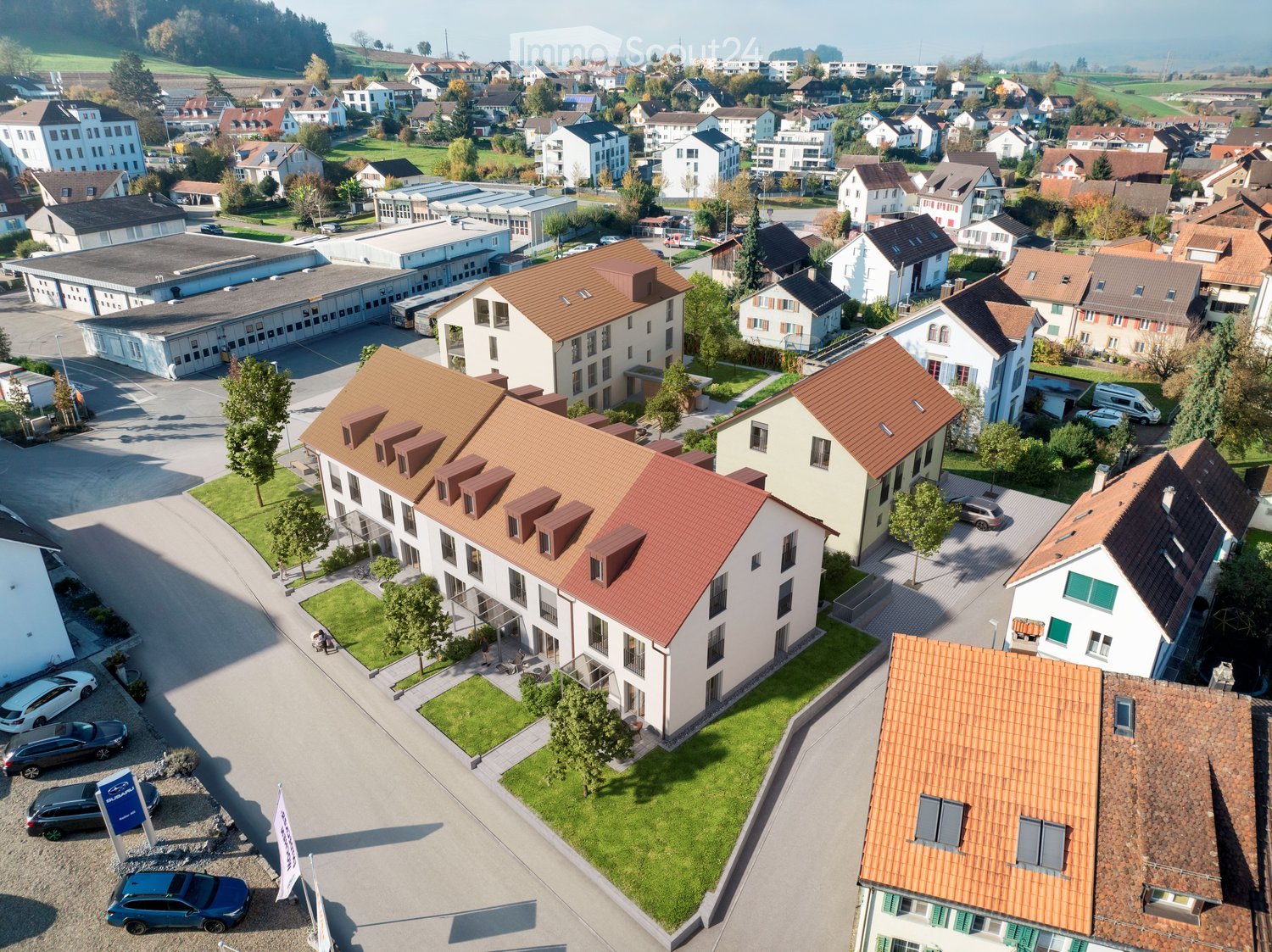 Aerial view of a residential area with multiple houses, a large building, and several cars parked in front of the houses.