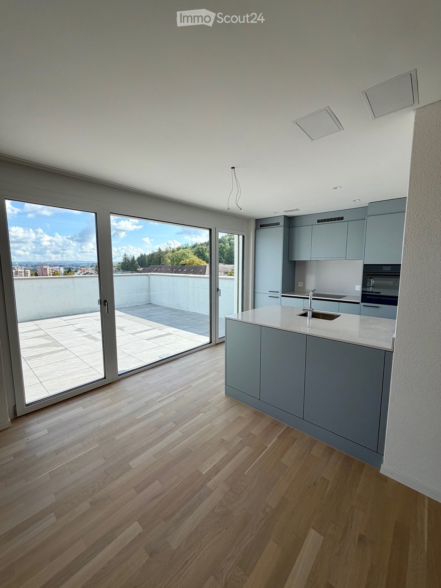 Modern kitchen with light grey cabinets, white countertop, and a large sliding glass door leading to a balcony.