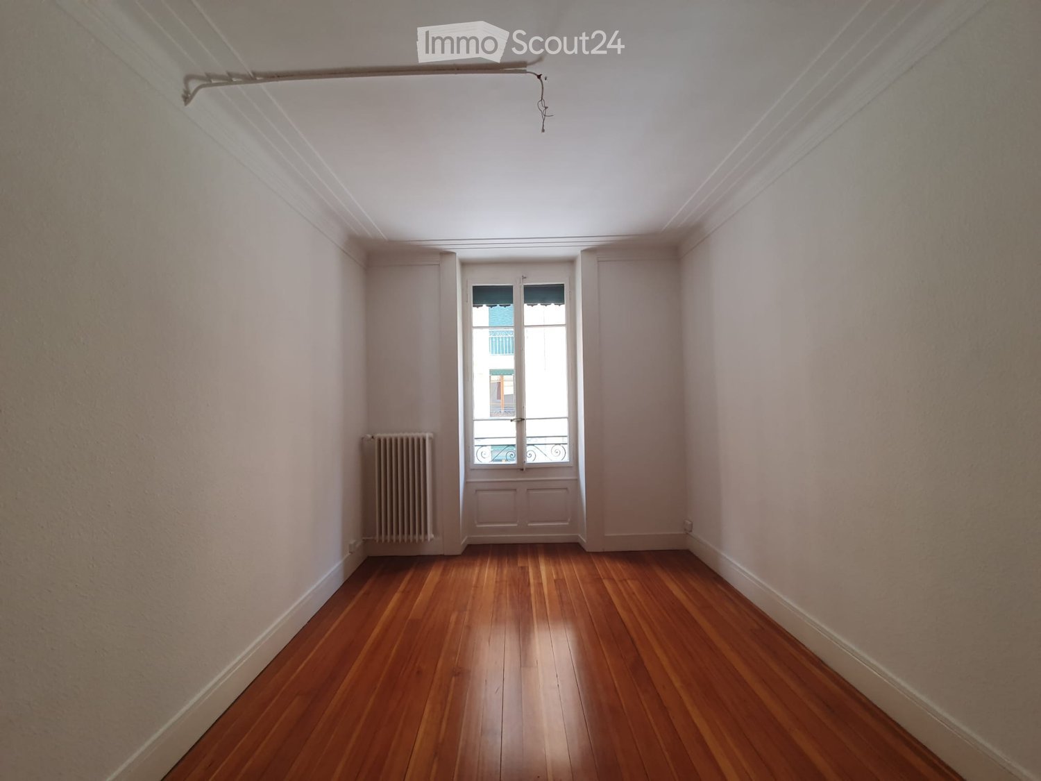 Empty room with wooden flooring, white walls, and a window with a radiator to the left.
