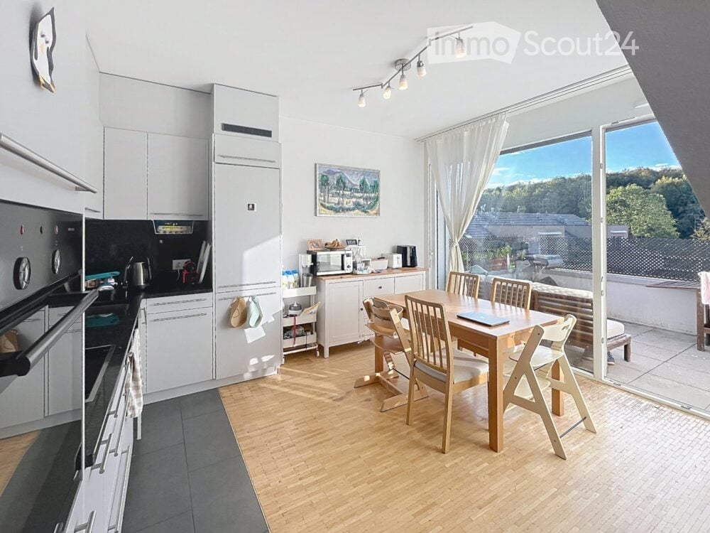 Open-plan kitchen and dining area with white cabinets, wooden flooring, and large windows offering a scenic view. Includes a dining table with chairs, a laptop, and various kitchen appliances.