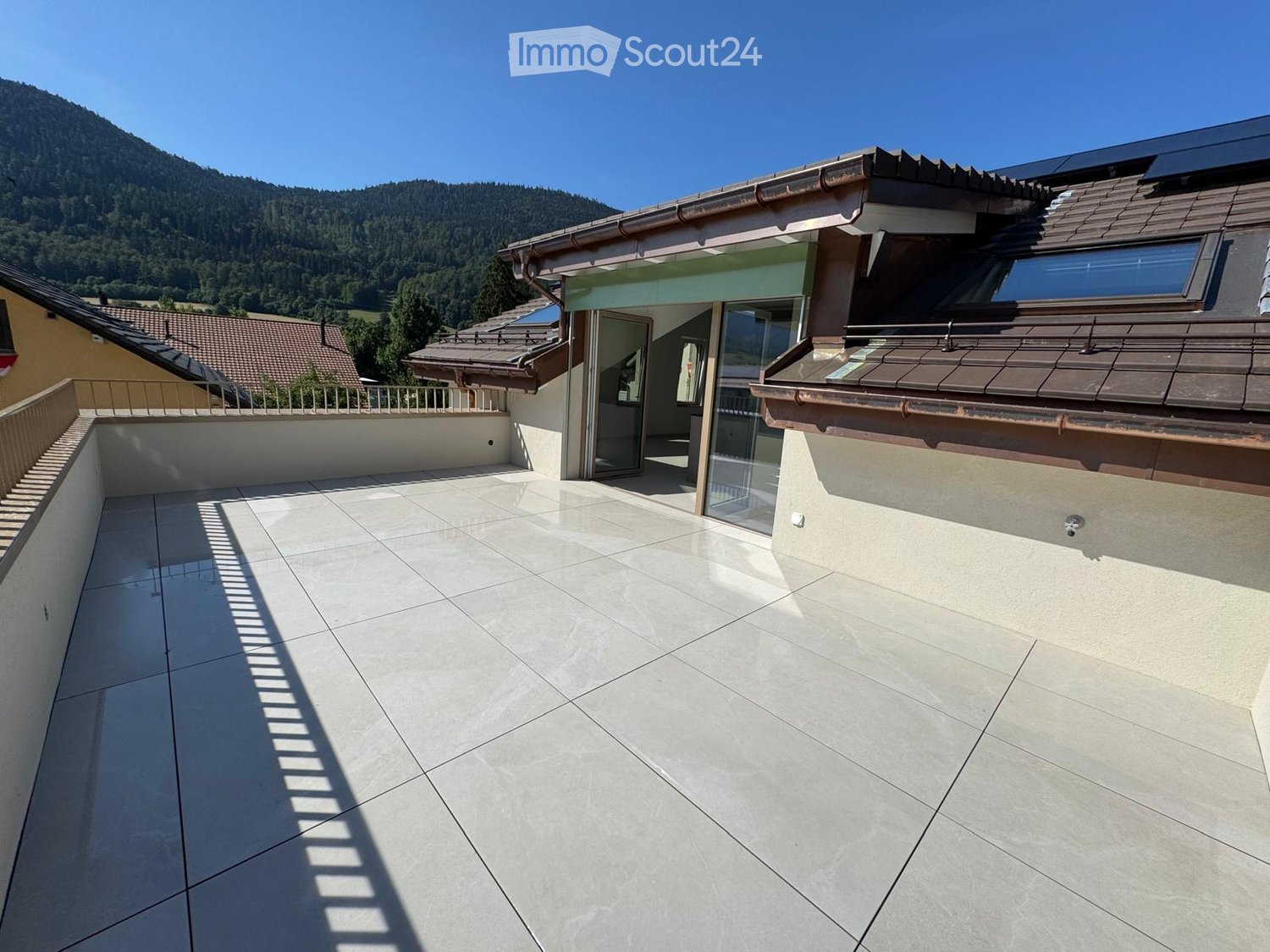 Roof terrace with large tiled floor, glass doors leading to the house, and a scenic mountain view in the background.