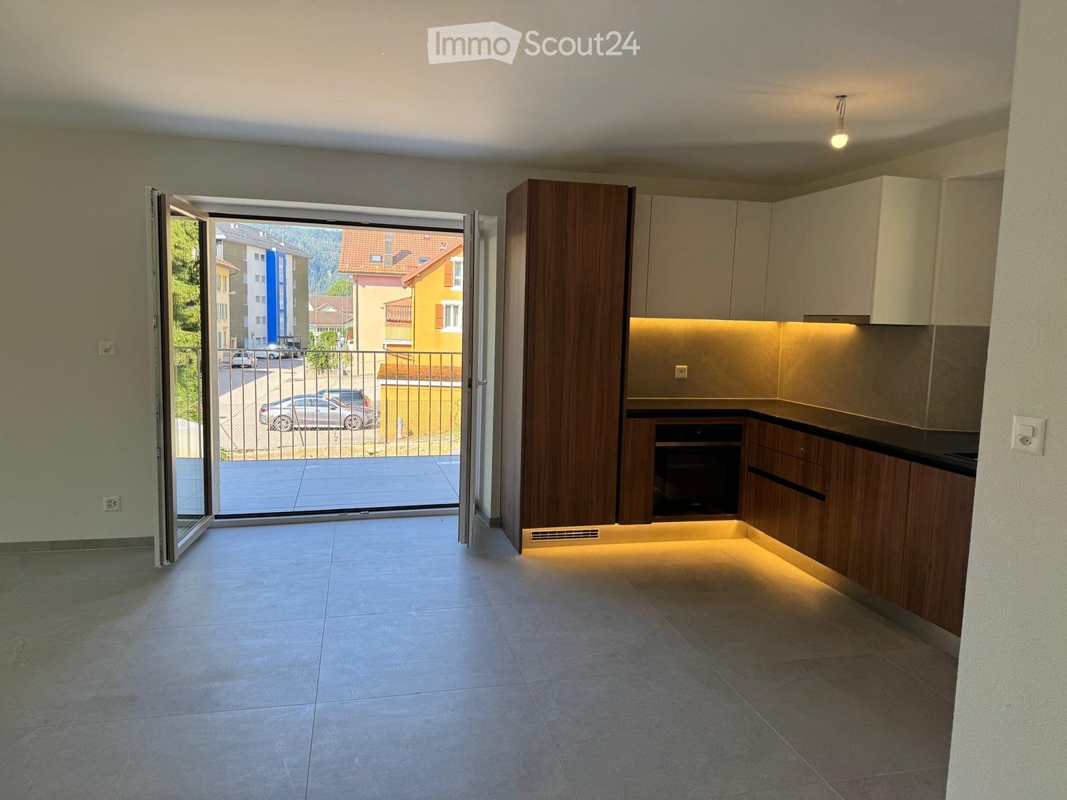 Modern kitchen with wooden cabinets, built-in oven, and a large sliding glass door leading to a balcony with a city view.