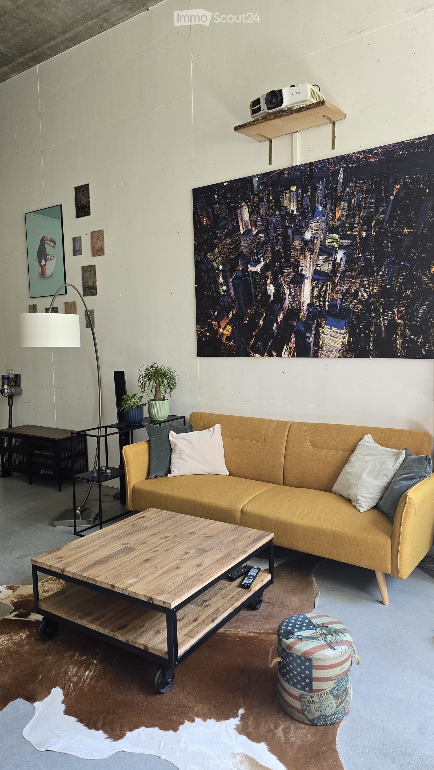 Modern living room with a mustard yellow sofa, wooden coffee table, floor lamp, and a large cityscape mural on the wall.
