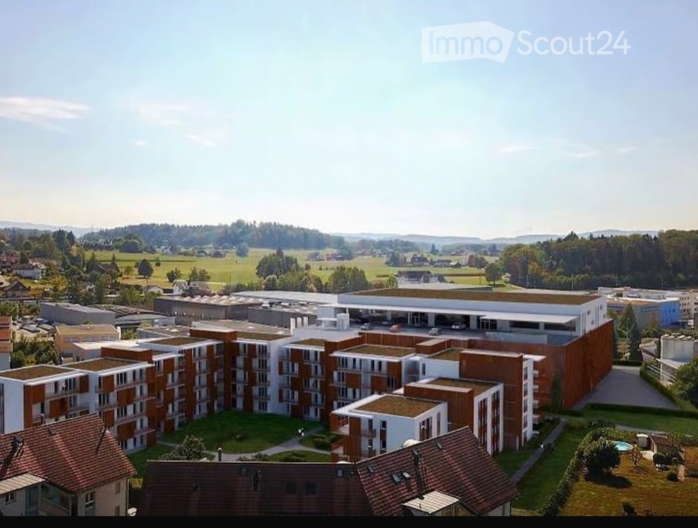 Aerial view of a modern residential complex with multiple apartment buildings, surrounded by green spaces and a parking area.