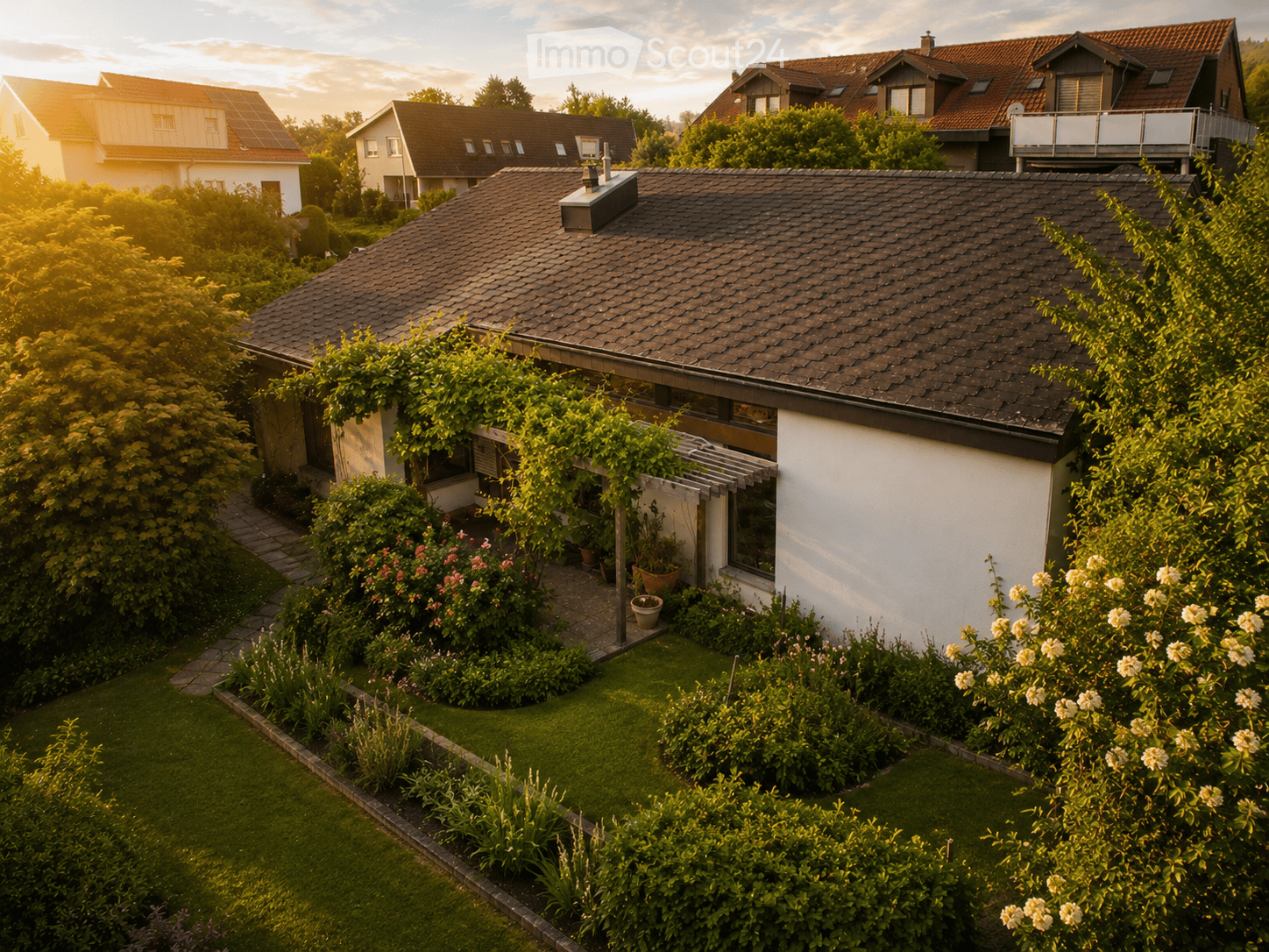 A well-maintained garden with a variety of plants, flowers, and a neatly trimmed lawn, surrounding a modern house with a tiled roof and white walls.