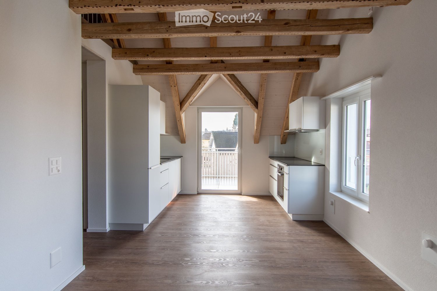 Bright, open kitchen with white cabinets, wooden beams on the ceiling, and a view to an outdoor area through a large glass door.