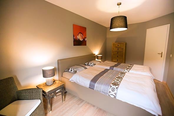 Cozy bedroom with a double bed, nightstands, a chair, and a wardrobe. The room features warm lighting and a modern aesthetic.