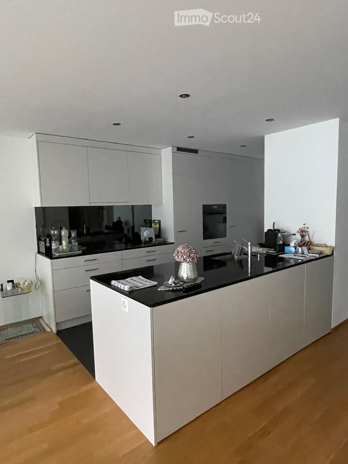 Modern kitchen with white cabinets, black countertops, and a central island. Features include a sink, faucet, oven, and decorative vase on the island.