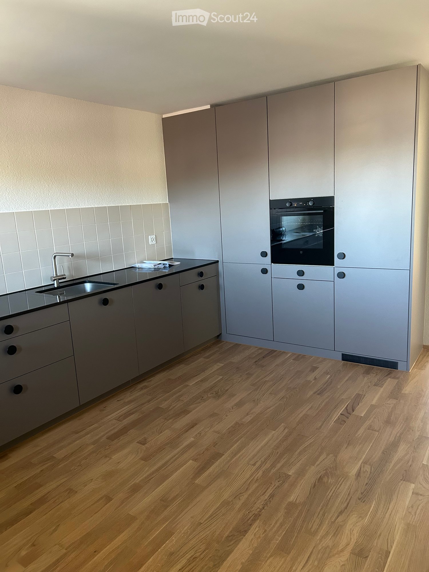 Modern kitchen with light grey cabinets, wooden flooring, and stainless steel sink and oven.