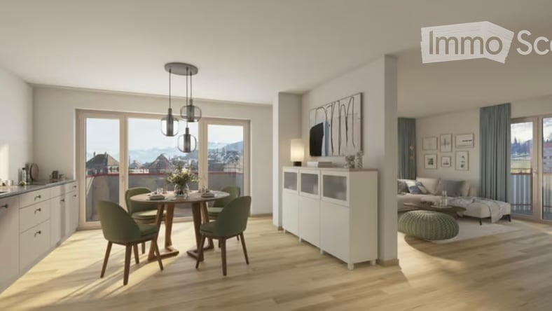 Modern, well-lit living and dining area with large windows offering a scenic view. Features a sofa, coffee table, dining table with chairs, a white cabinet, wall-mounted TV, floor lamp, and decorative picture frames.