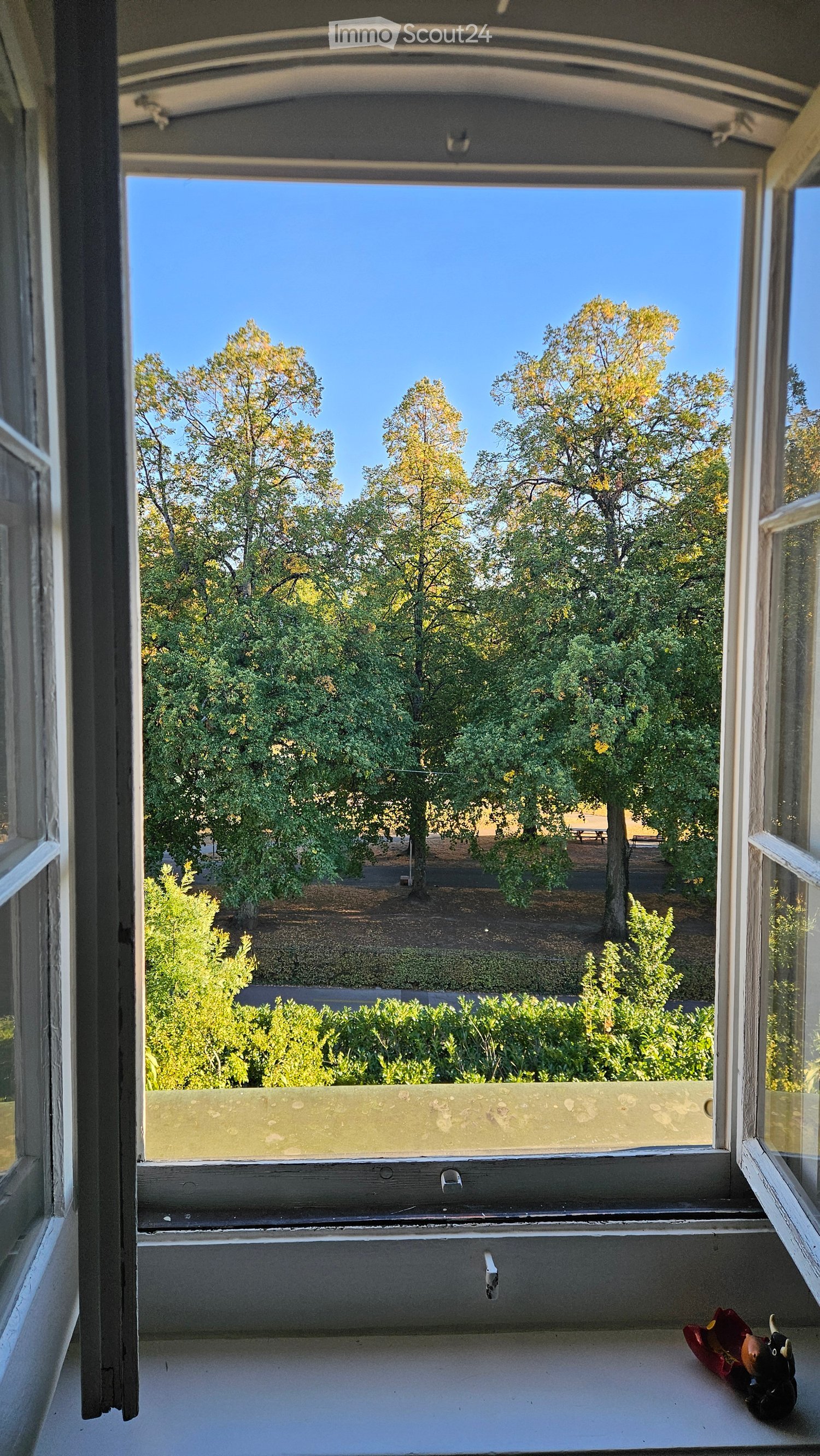 Balcony with a view of trees and a park, featuring a small statue on the windowsill.
