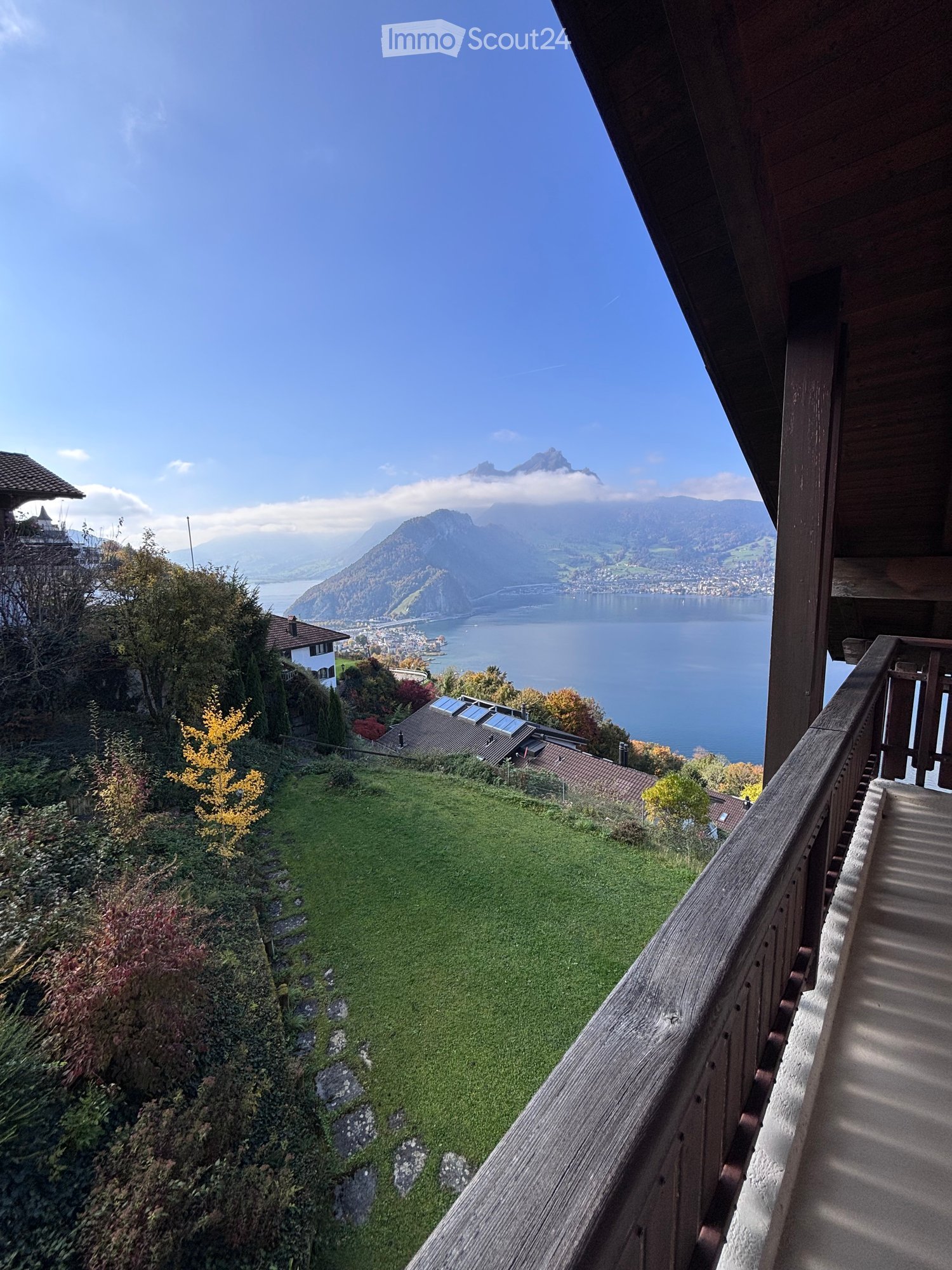 Balcony overlooking a scenic lake and mountain landscape with a grassy slope below.