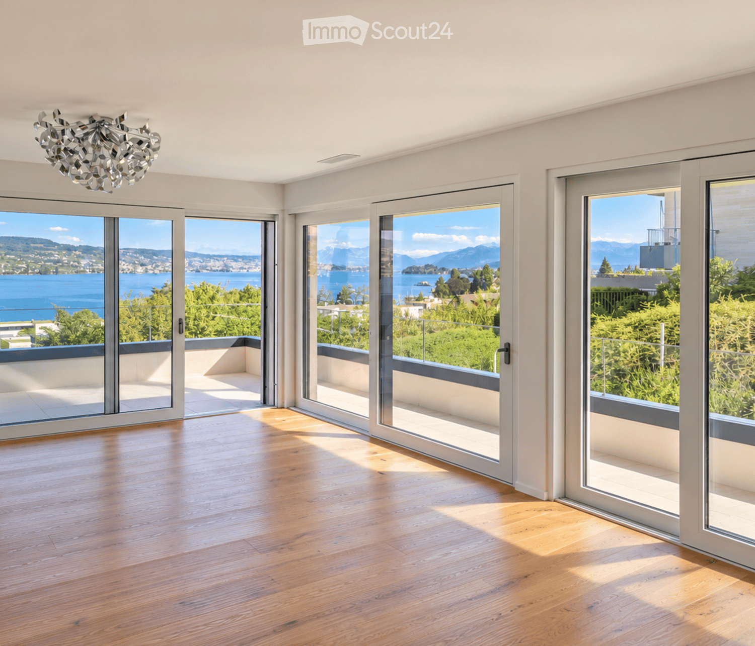 Bright, empty room with large glass sliding doors opening to a balcony, wooden floor, and a view of a lake and mountains.
