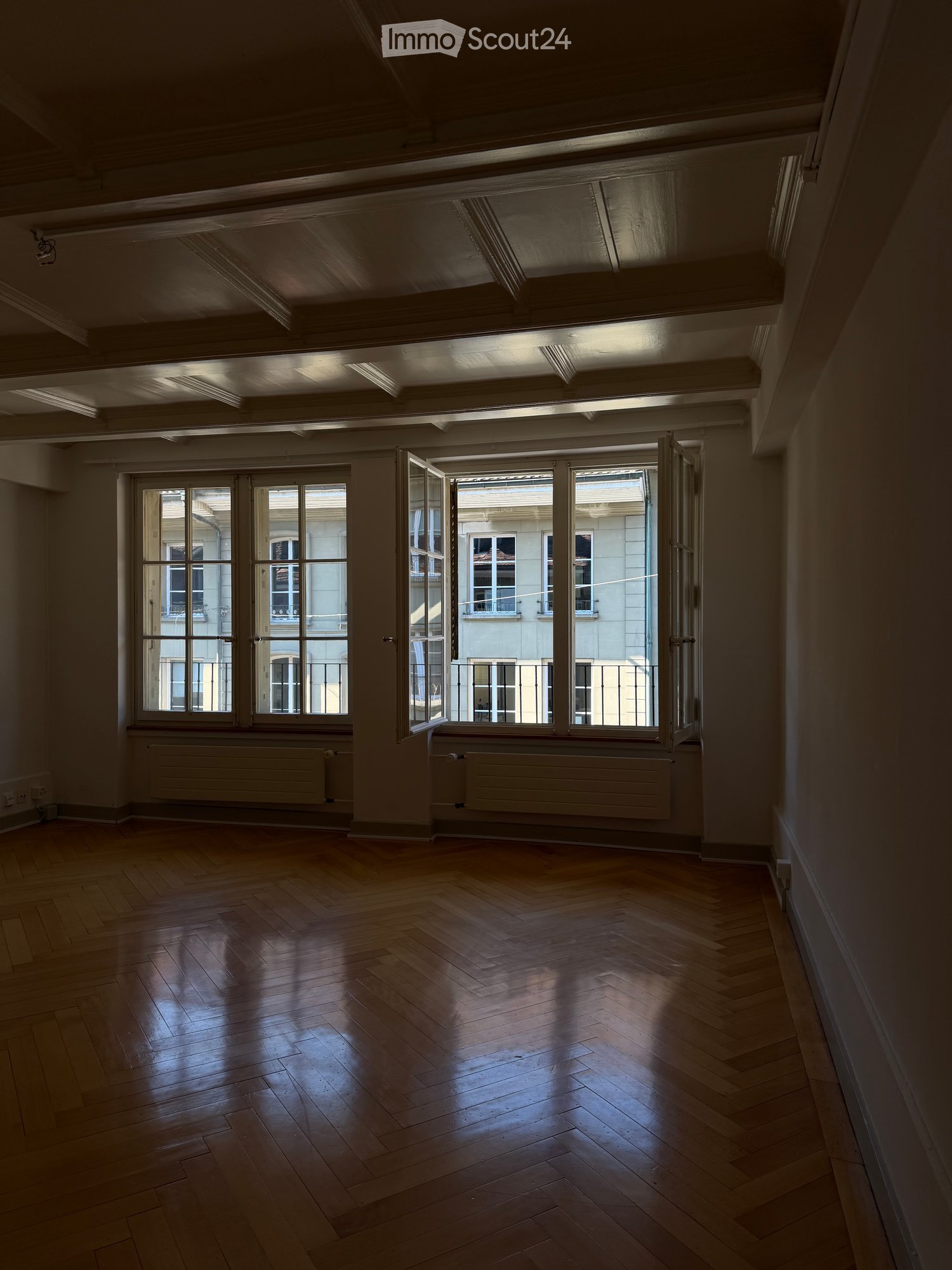 Empty room with wooden flooring, large windows, and radiators. No furniture or equipment present.