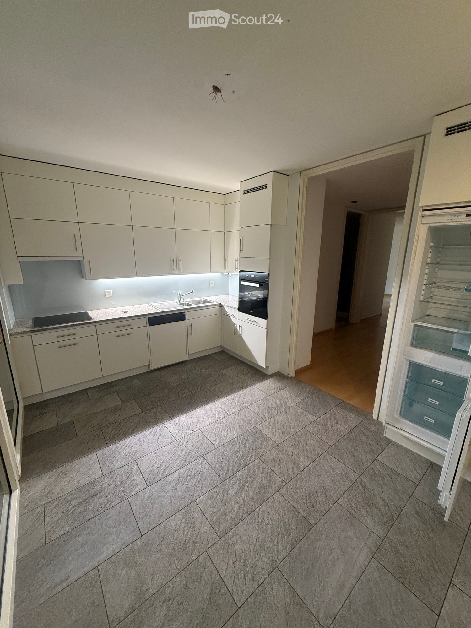 Modern kitchen with white cabinets, stainless steel appliances, and grey tiled flooring.