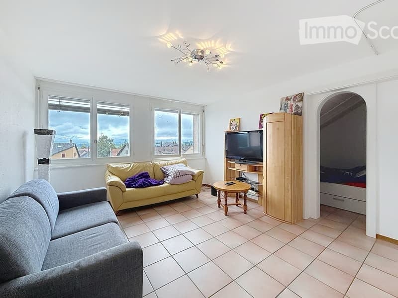 Bright living room with large windows, two sofas, a coffee table, a TV on a stand, and a wooden wardrobe.