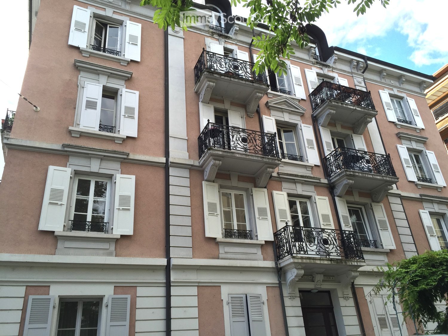 Multi-story building with pink facade, white shutters, and multiple balconies with black wrought-iron railings.