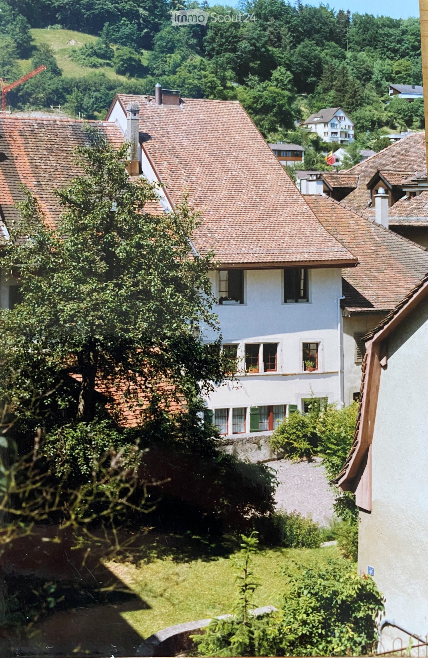 A view of a residential area with multiple houses featuring red-tiled roofs and white walls, surrounded by greenery and trees.