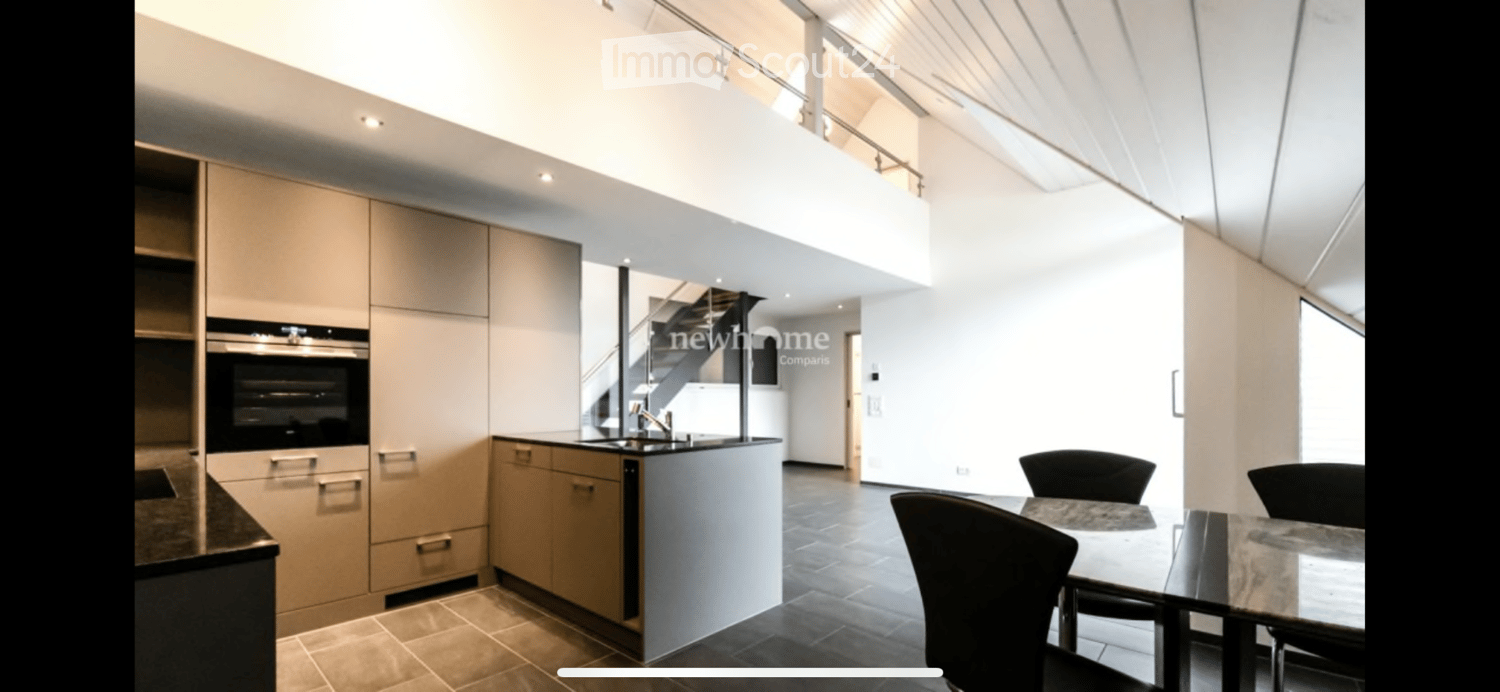 Modern kitchen with light-colored cabinets, built-in oven, and a small dining area with a table and chairs. The space features a sleek, contemporary design with a raised platform leading to an upper level.