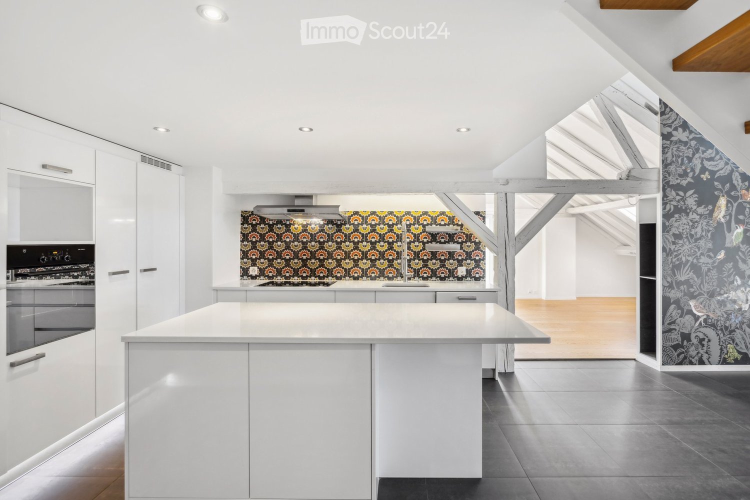 Modern kitchen with white cabinets, central island, stainless steel oven, and colorful backsplash.