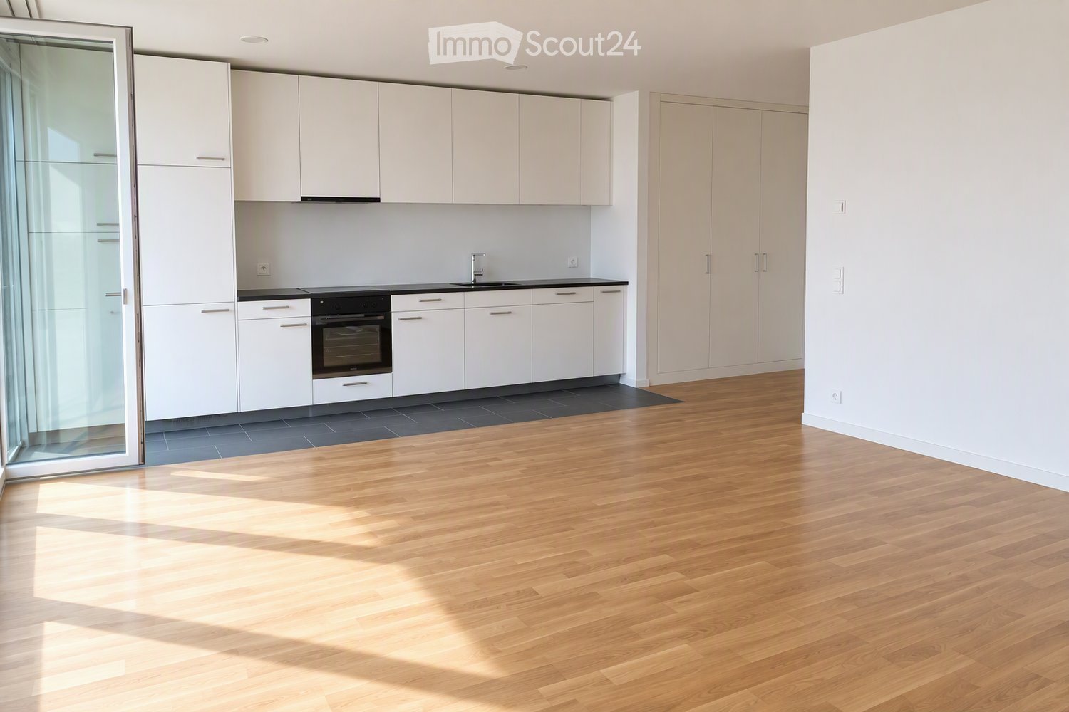 Modern kitchen with white cabinets, a sink, and an oven, featuring wooden flooring and large windows allowing natural light to fill the space.
