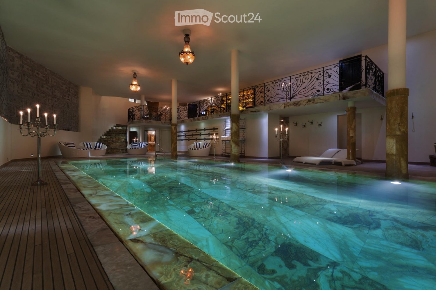 Indoor swimming pool area with lounge chairs, decorative columns, and chandeliers.